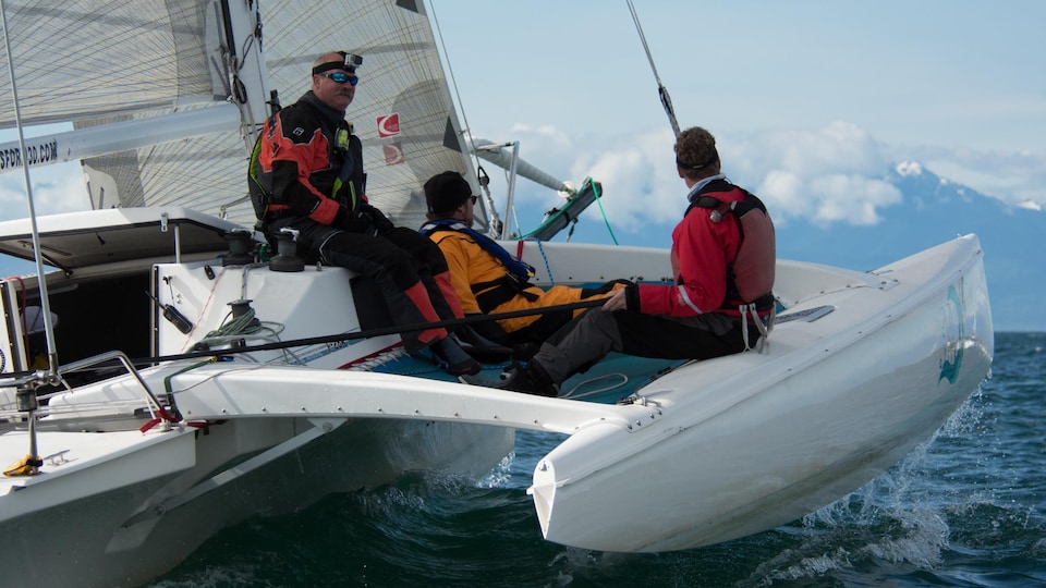 Trois matelots sont assis sur un catamaran en pleine navigation.