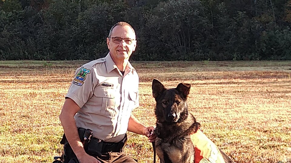 Un homme est à genoux à l'extérieur et tient la laisse de son chien en souriant.
