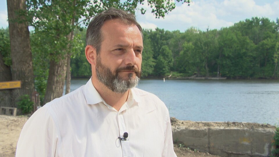 Sylvain Gariépy accorde une entrevue à Radio-Canada à proximité d'un cours d'eau en été.
