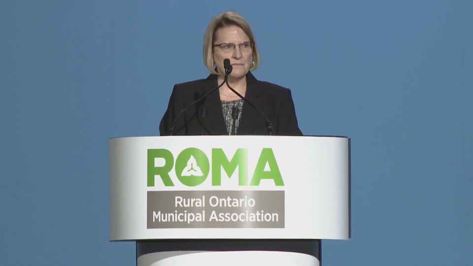 Sylvia Jones est debout derrière un lutrin aux couleurs de l'Association des municipalités rurales de l'Ontario.