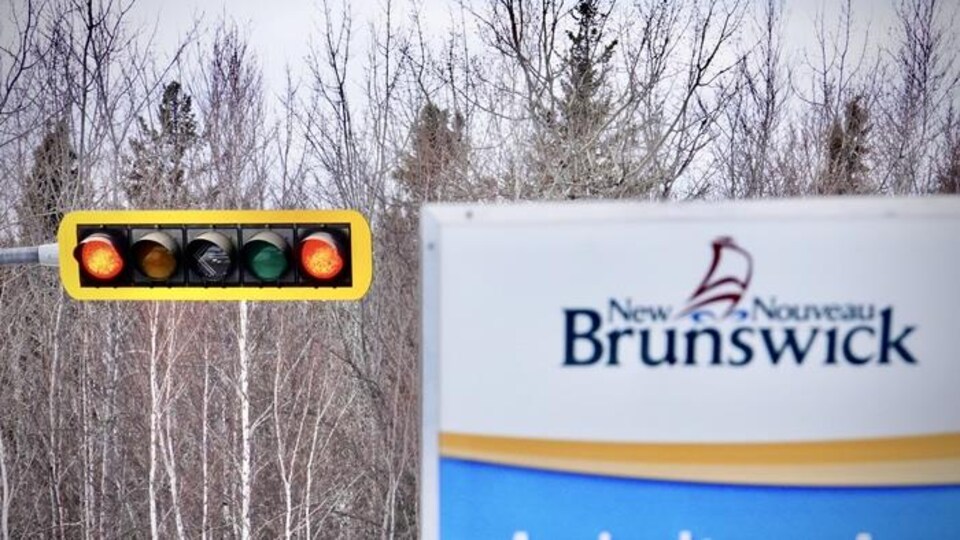 Un feu de circulation au rouge, à côté d'une pancarte indiquant le Nouveau-Brunswick.