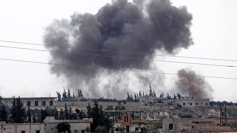 Un nuage de fumée noire plane au-dessus de bâtiments dévastés par un bombardement en Syrie.