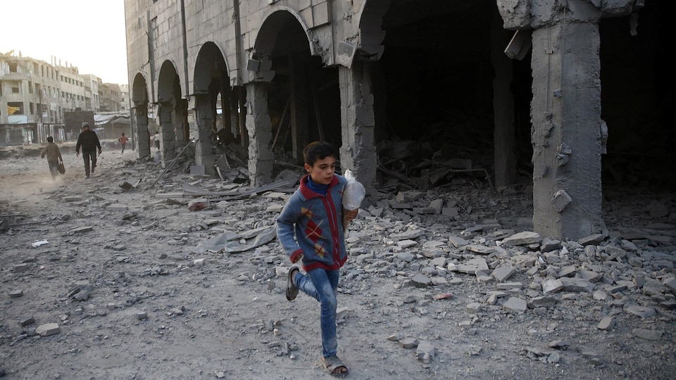 Un garçon syrien court près d'un immeuble endommagé.