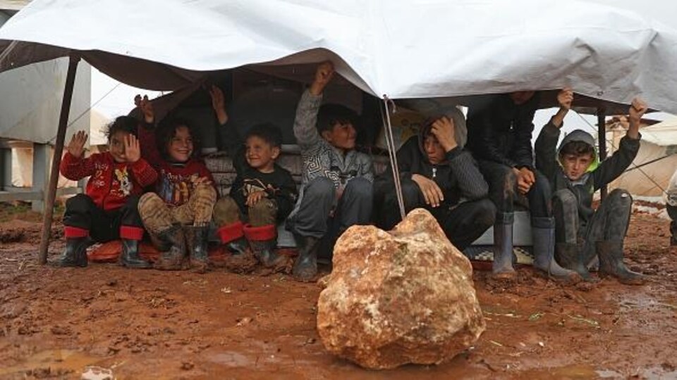 Des enfants syriens souriant sous une tente dans un camp pour personnes déplacées. 