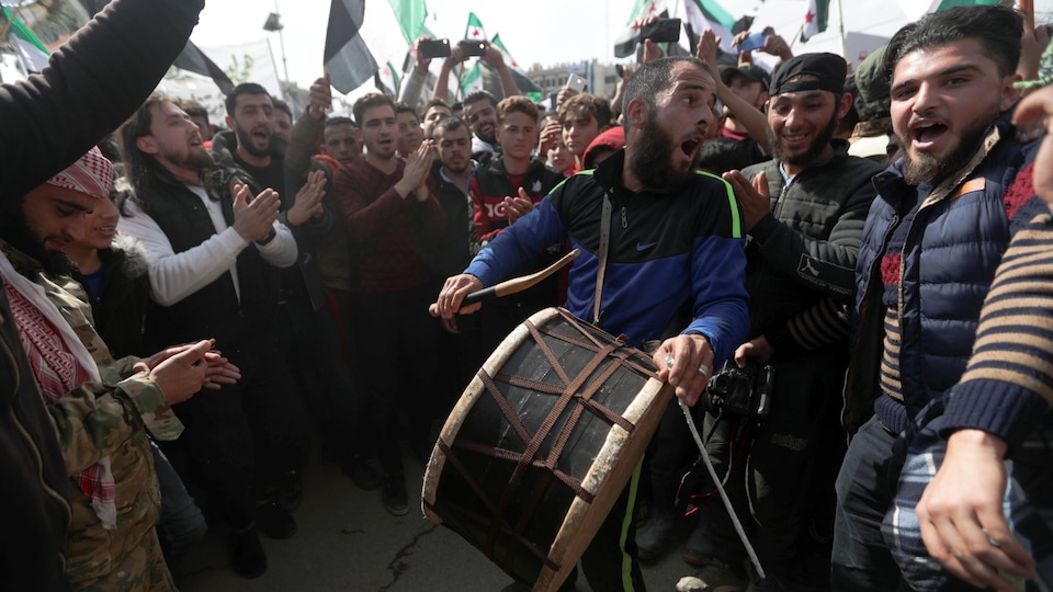 Un homme tapant sur un tambour entouré d'hommes.