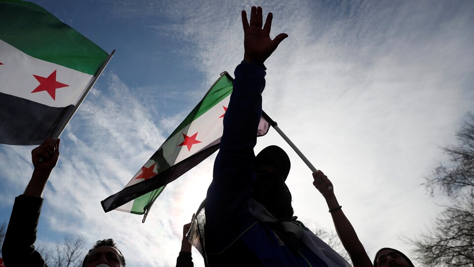 Des gens qui portent des drapeaux syriens manifestent.