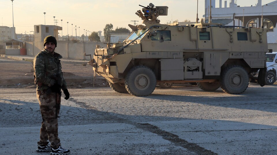 Un combattant en treillis militaire, près d'un véhicule blindé.