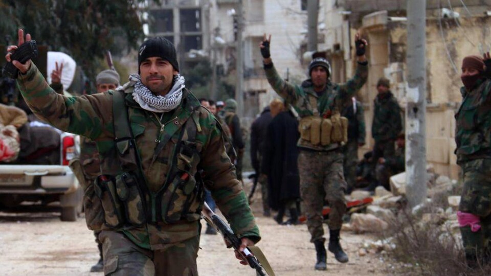 Des soldats de l'armée syrienne font le signe de la victoire dans une rue. 