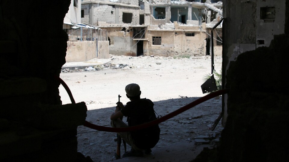 Un soldat est accroupi dans l'entrée d'un immeuble et regarde la ville au loin.