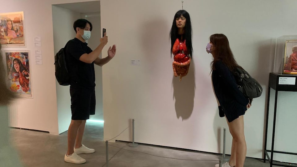 Un homme photographie une femme devant une sculpture.