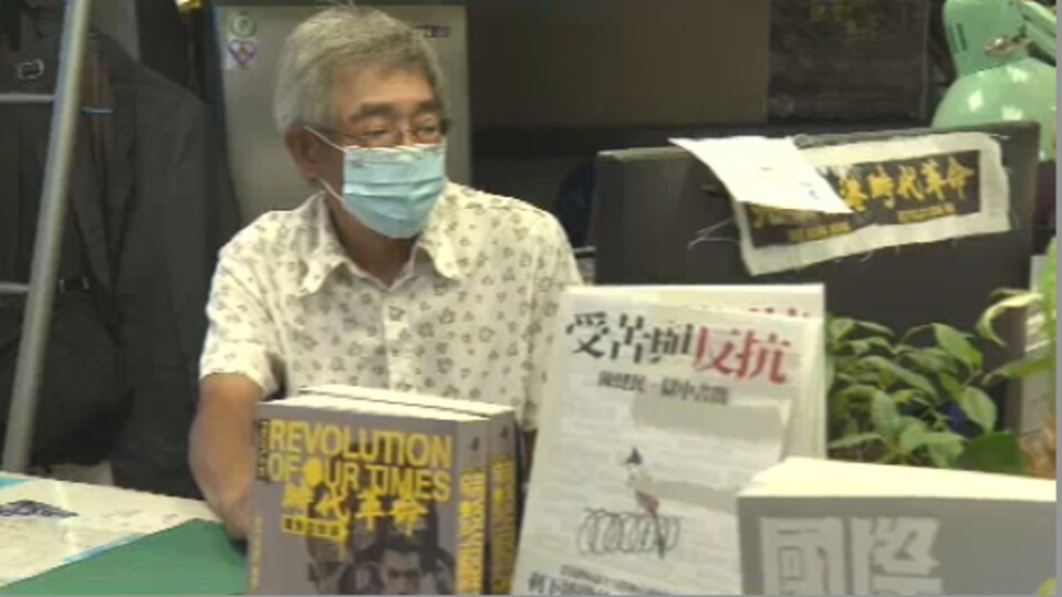 Lam Wing Kee assis à une table, des livres posés devant lui. 