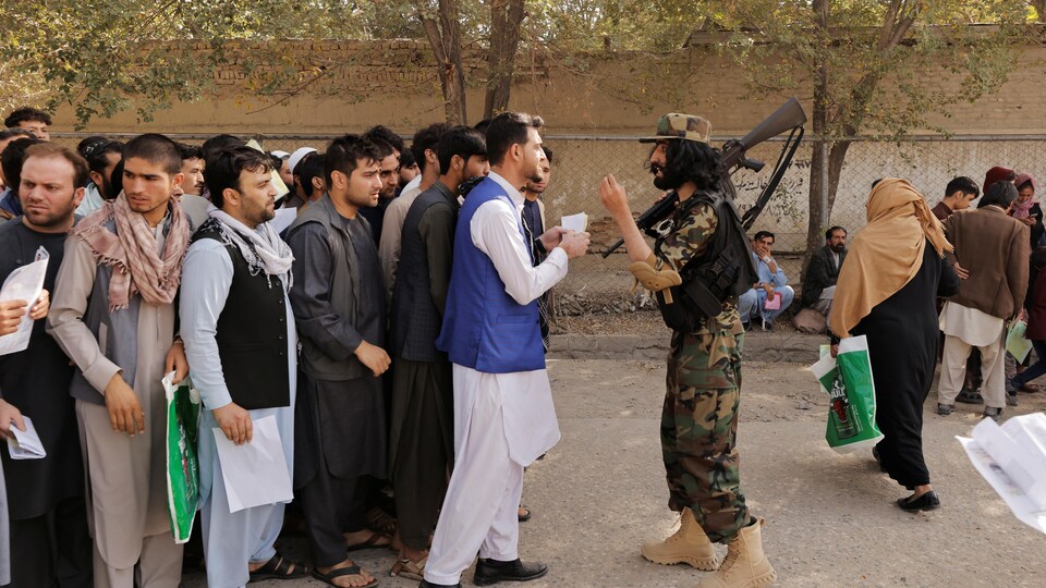 Une foule d'hommes se tient devant un soldat taliban qui transporte une mitraillette sur son épaule.