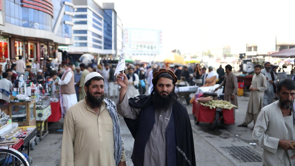 Un homme agite le drapeau taliban au milieu d'une rue commerçante.