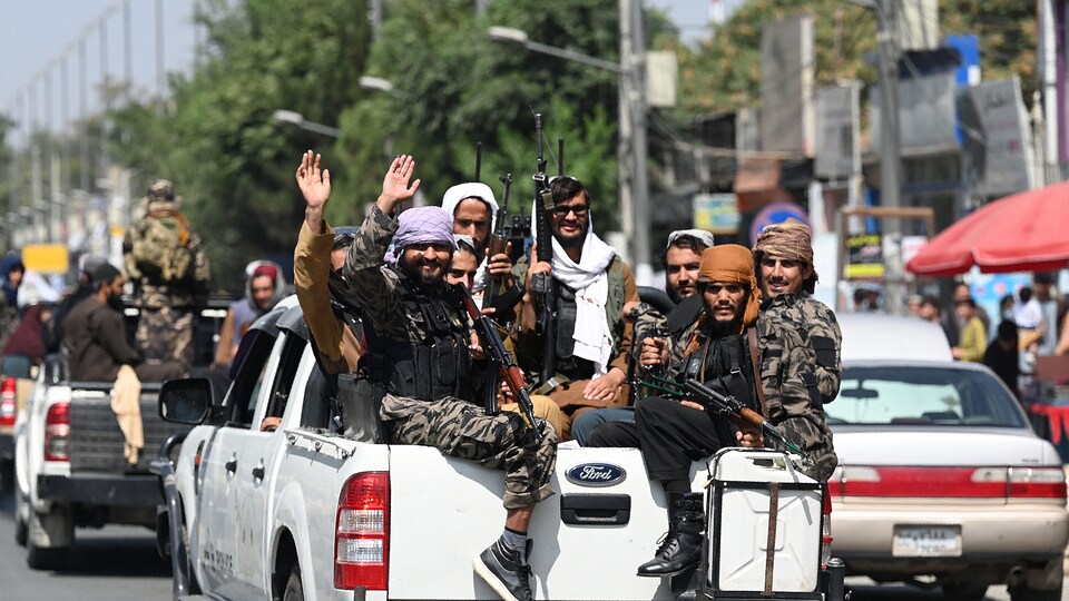 Des talibans dans une camionnette font des signes de la main.