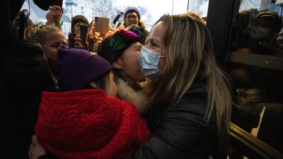 Une femme avec un masque serre dans ses bras des gens dans une foule.