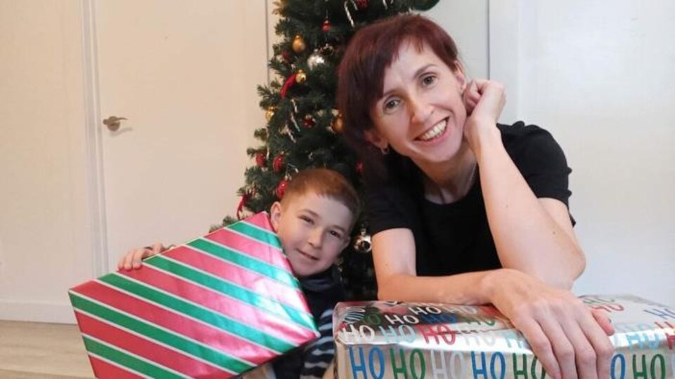 Tamara i jej chłopiec uśmiechają się przed choinką i rozdają prezenty.