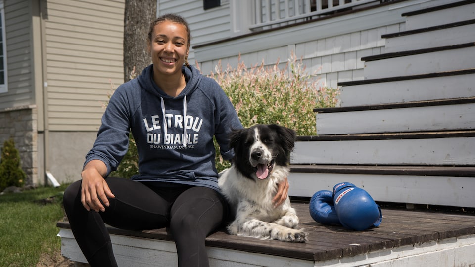 Tammara Thibeault assise sur les marches d'une maison avec son chien et des gants de boxe à côté.