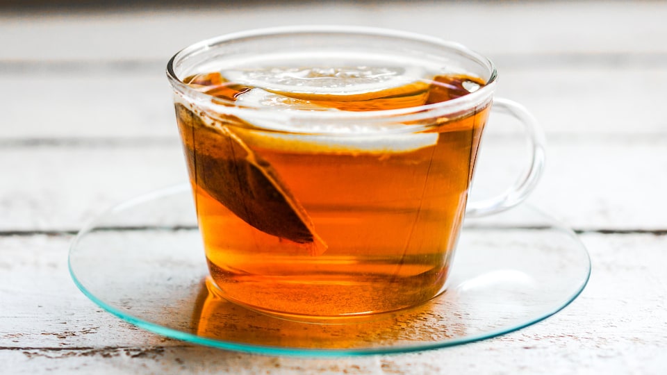 Un sachet de thé infuse dans une tasse transparente.