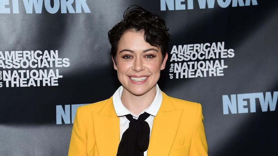Une femme souriante devant un affiche indiquant «American Associate of the National Theater». 