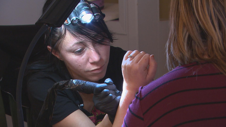 Une femme fait un tatouage sur le poignet d'une autre femme.