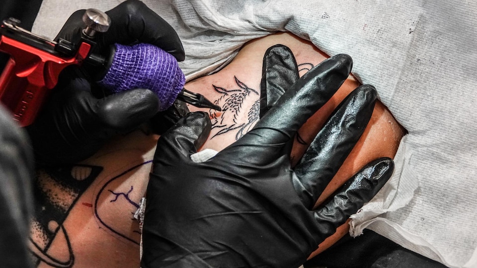 Un tatoueur dessine une abeille sur le bras d'une femme.