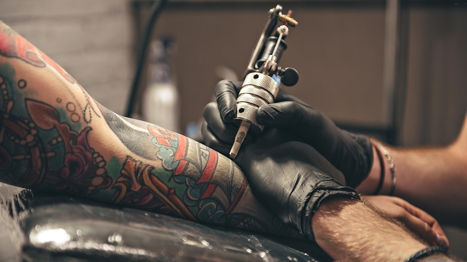 Une personne qui tient un outil permettant de faire des tatouages fait un dessin sur le bras d'une autre personne.