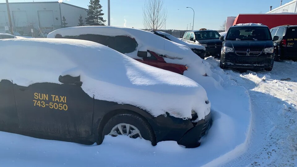 Des voitures de la société Sun Taxi garées sous la neige dans un stationnement.