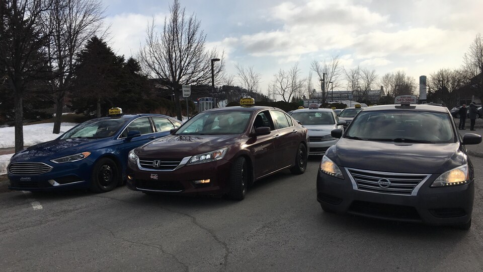 Trois voitures taxi stationnées une à côté de l'autre en attendant de commencer à circuler sur trois voies de circulation.