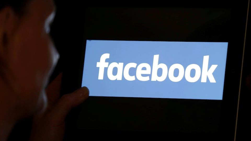 Une femme regardant le logo de Facebook sur une tablette électronique.