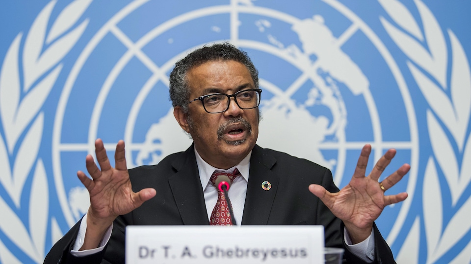 Tedros Adhanom Ghebreyesus parle dans un micro devant un immense logo des Nations unies. 