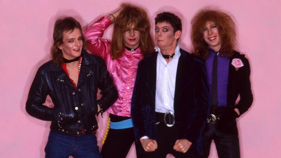 Quatre hommes prennent la pose devant un fond rose.
