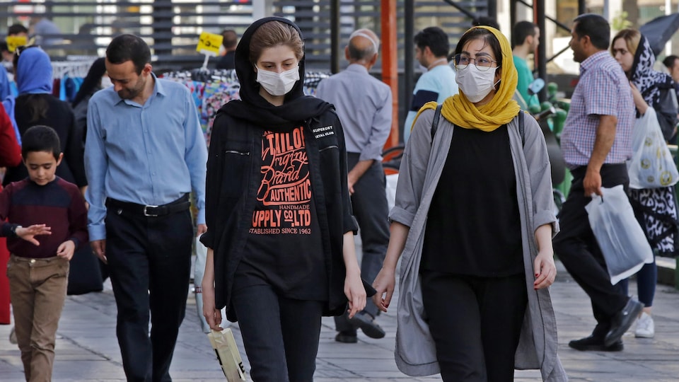 Des femmes et des hommes, dont certains portent des masques de protection, circulent  dans une de la capitale iranienne.