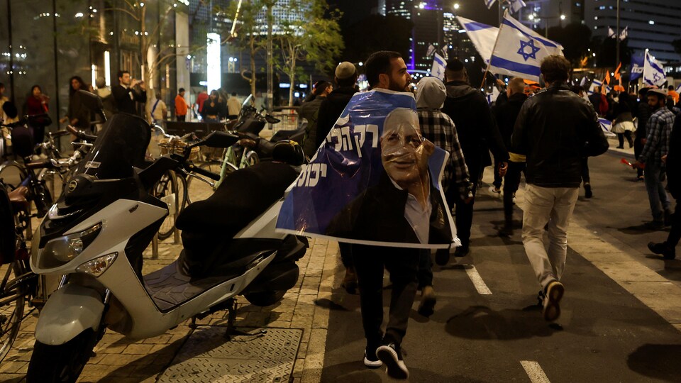 Des personnes manifestent dans une rue avec des drapeaux israéliens et des affiches.