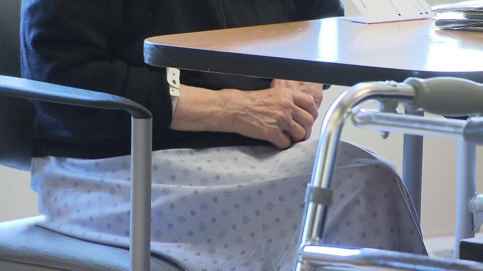 Mains d'une personne âgée assise à une table à côté de sa marchette.