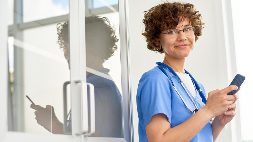 Portrait d'une médecin regardant la caméra et tenant un téléphone cellulaire dans ses mains.