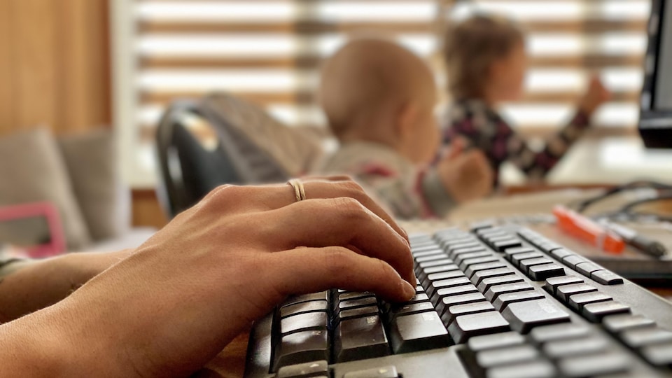 Gros plan d'une main sur un clavier avec des enfants à l'arrière-plan.