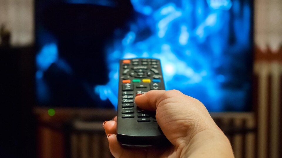 Une main tient une télécommande devant un écran de télévision.