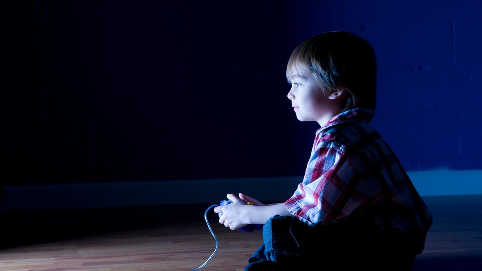 Un enfant avec une manette devant un écran.