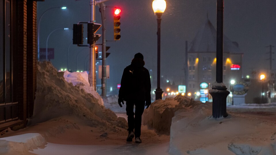 Une personne marche sur un trottoir enneigé du centre-ville de Moncton. 