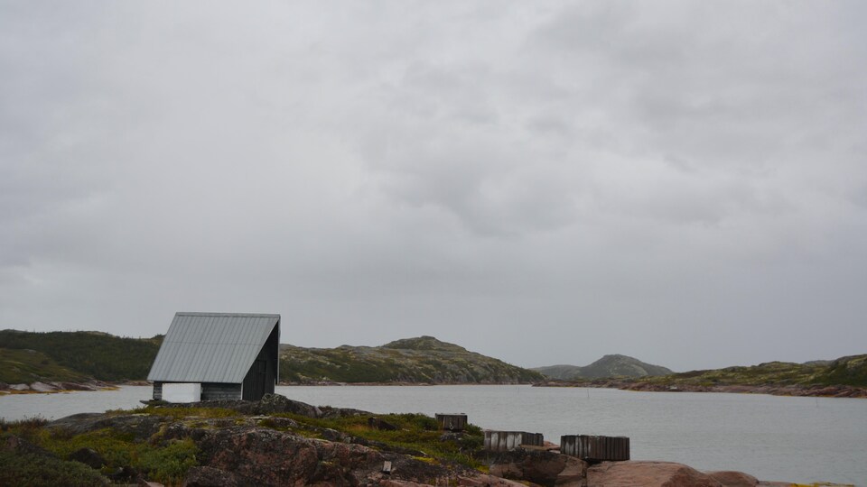 Une cabane en bois sur le bord de l'eau avec un ciel gris.