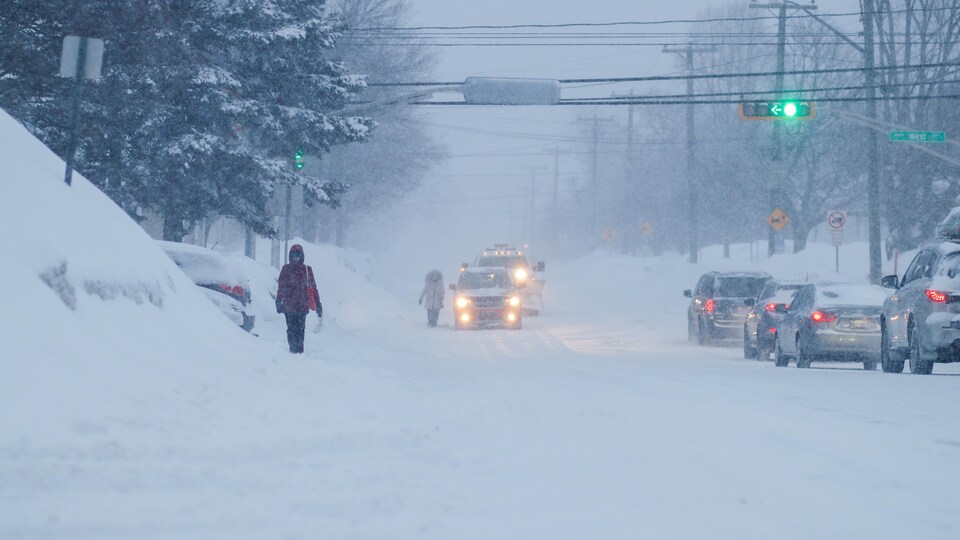 Des femmes marchent dans la tempête parmi les automobiles.
