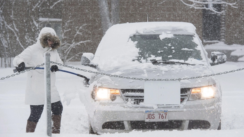 Une femme déneige sa voiture pendant une tempête de neige au Nouveau-Brunswick en janvier 2018.