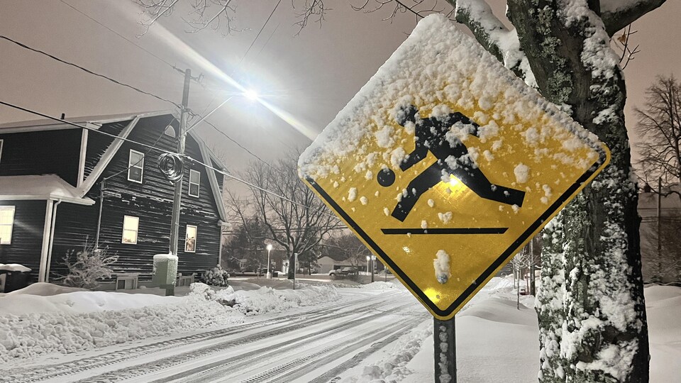 Un panneau appelant les automobilistes à faire attention aux enfants qui jouent dans la rue est recouvert de neige.