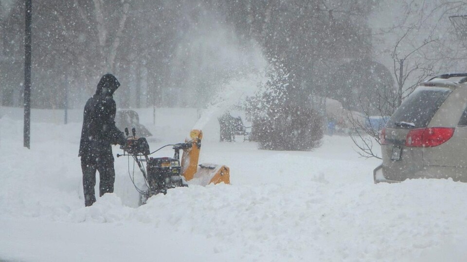 Un homme enlève la neige avec sa souffleuse.
