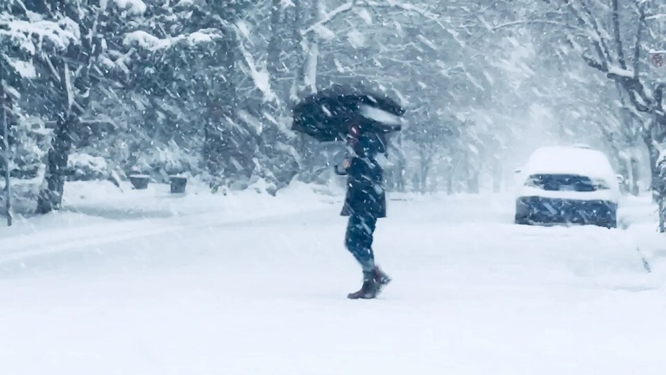Une personne tenant un parapluie ouvert traverse une rue lors d'une tempête de neige.