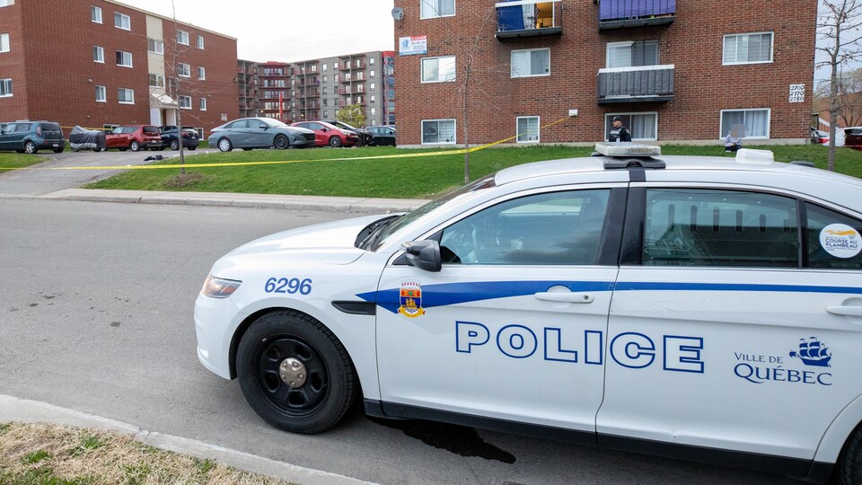 Une voiture de police stationnée devant un complexe d'immeubles à logements.
