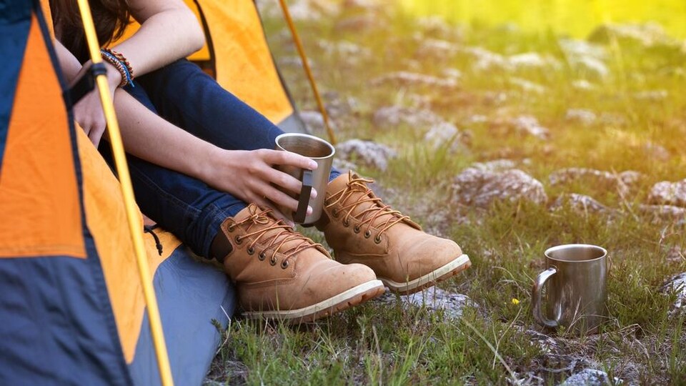 Une campeuse boit un café à l'entrée d'une tente.