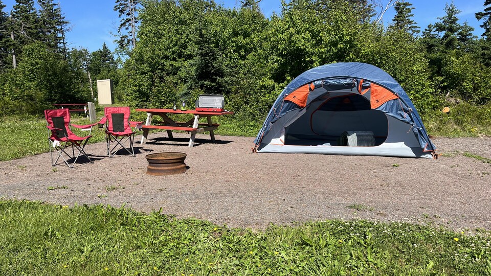 Une tente, des chaises et un réchaud de camping sont disposés sur un site du terrain de Stanhope.
