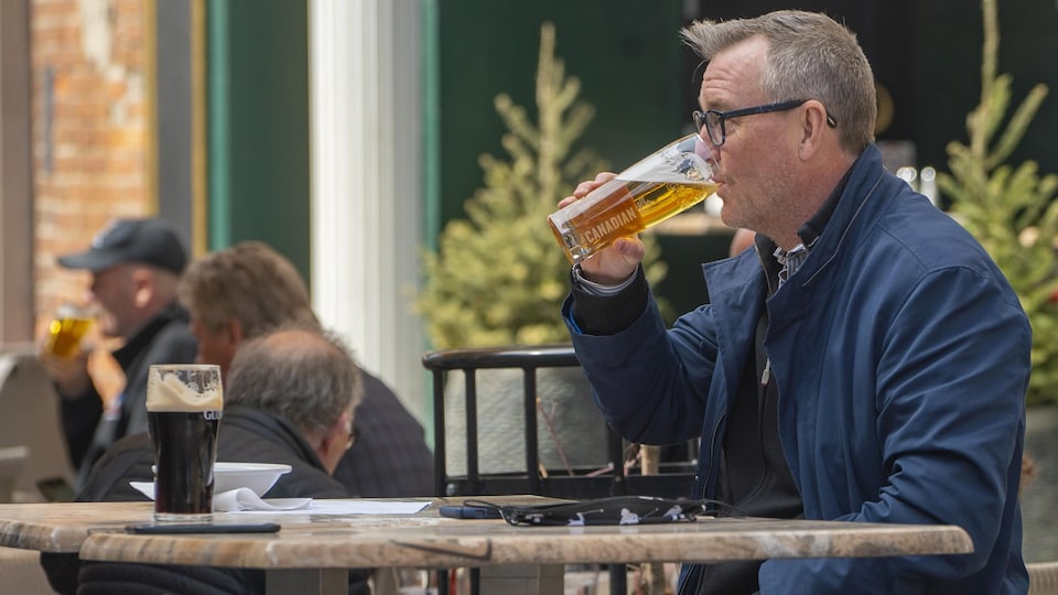 Un homme boit de la bière, installé à la terrasse d'un restaurant.