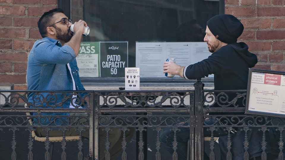 Deux hommes attablés à une terrasse boivent une bière.